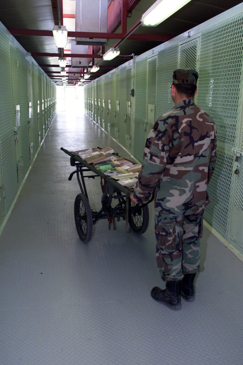 Typical Camp Delta detention facility cell block corridor with a guard carrying reading material for the detainees