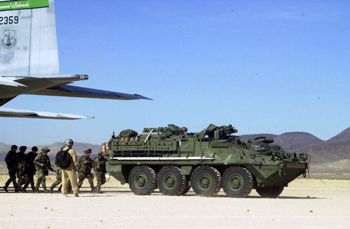 A Stryker Infantry Carrier Vehicle squad follows their vehicle out of an Air Force C130 Hercules aircraft after landing at Bicycle Lake Army Airfield at the National Training Center, Fort Irwin, California.