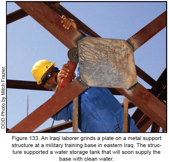 Figure 133. An Iraqi laborer grinds a plate on a metal support structure at a military training base in eastern Iraq. The structure supported a water storage tank that will soon supply the base with clean water.