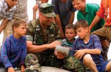Photo showing U.S. Marine Corps Capt. Robert A. Riggle plays tic-tac-toe with a group of Albanian boys in Camp Hop