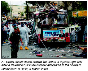 An Israeli soldier walks behind the debris of a passenger bus after a Palestinian suicide bomber attacked it in the northern Israeli town of Haifa, 5 March 2003.