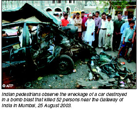 Indian pedestrians observe the wreckage of a car destroyed in a bomb blast that killed 52 persons near the Gateway of India in Bombay, 26 August 2003.